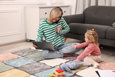 Photo of Work at home. Single mother talking by smartphone and her daughter on floor indoors