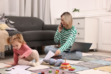 Photo of Work at home. Single mother talking by smartphone and her daughter on floor indoors