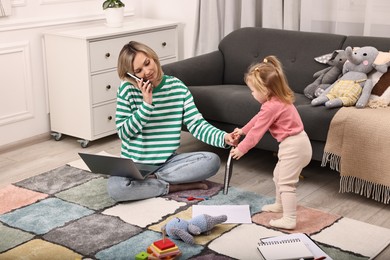 Photo of Work at home. Single mother talking by smartphone and her daughter on floor indoors