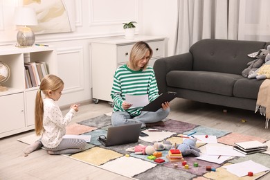 Photo of Single mother doing paperwork and her daughter on floor at home