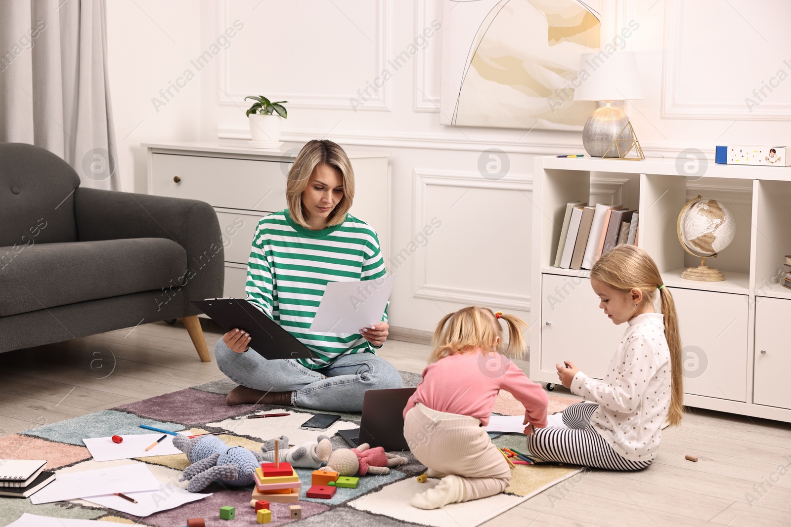 Photo of Single mother working and her children playing on floor at home