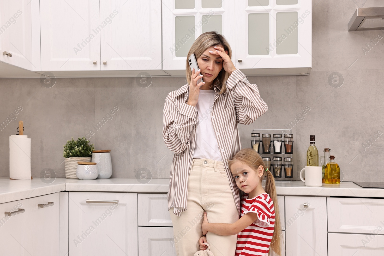 Photo of Work at home. Overwhelmed single mother talking by smartphone and her daughter in kitchen