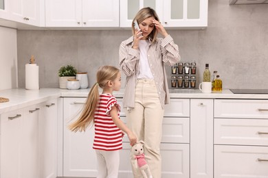 Photo of Work at home. Overwhelmed single mother talking by smartphone and her daughter in kitchen