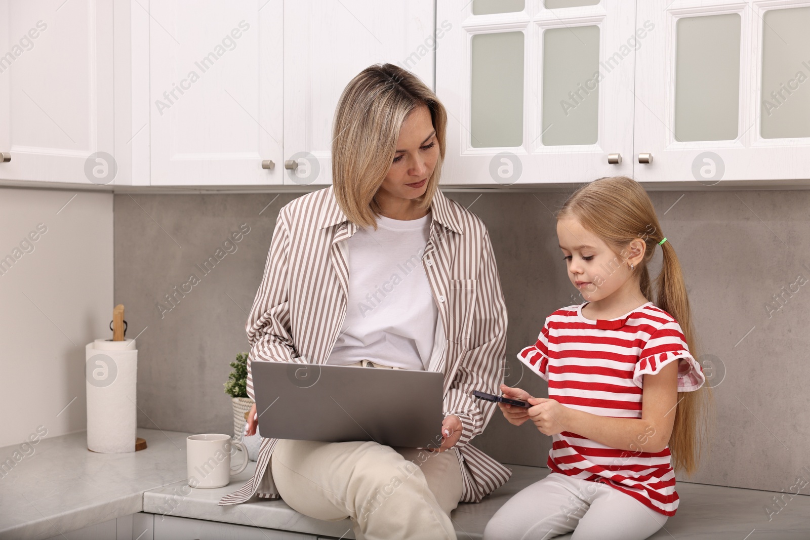 Photo of Single mother working with laptop and her daughter in kitchen