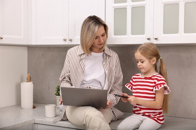 Photo of Single mother working with laptop and her daughter in kitchen