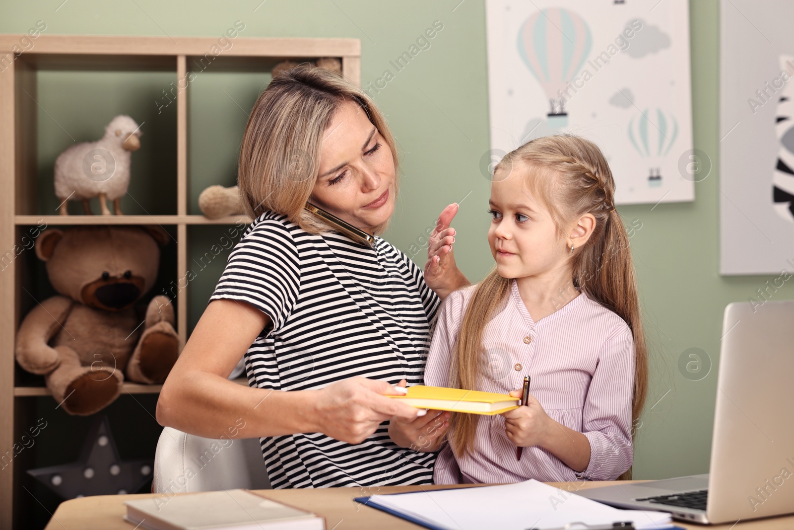 Photo of Work-family balance. Single mother talking by smartphone and her daughter at table in child's room