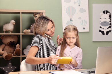 Photo of Work-family balance. Single mother talking by smartphone and her daughter at table in child's room