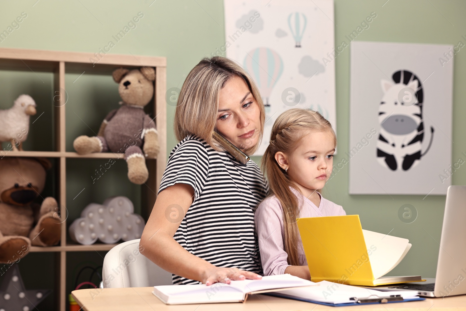 Photo of Work-family balance. Single mother talking by smartphone and her daughter at table in child's room