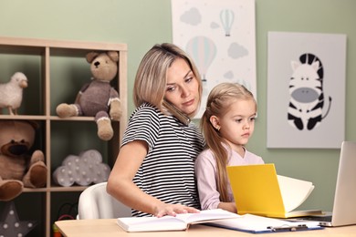 Photo of Work-family balance. Single mother talking by smartphone and her daughter at table in child's room