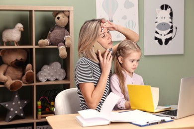 Photo of Work-family balance. Overwhelmed single mother talking by smartphone and her daughter at table in child's room