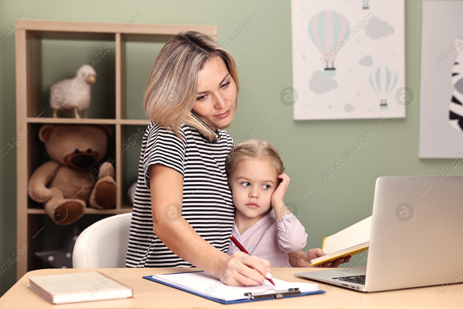 Photo of Work-family balance. Single mother talking by smartphone and her daughter at table in child's room