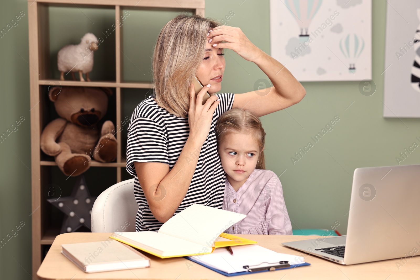 Photo of Work-family balance. Overwhelmed single mother talking by smartphone and her daughter at table in child's room