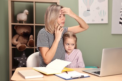 Photo of Work-family balance. Overwhelmed single mother talking by smartphone and her daughter at table in child's room