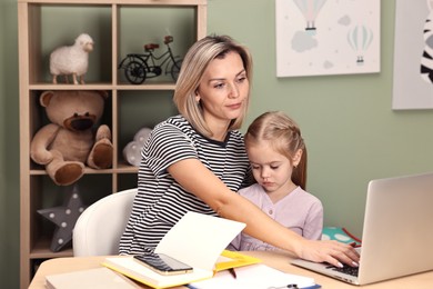 Photo of Overwhelmed single mother working with laptop and her daughter at table in child's room