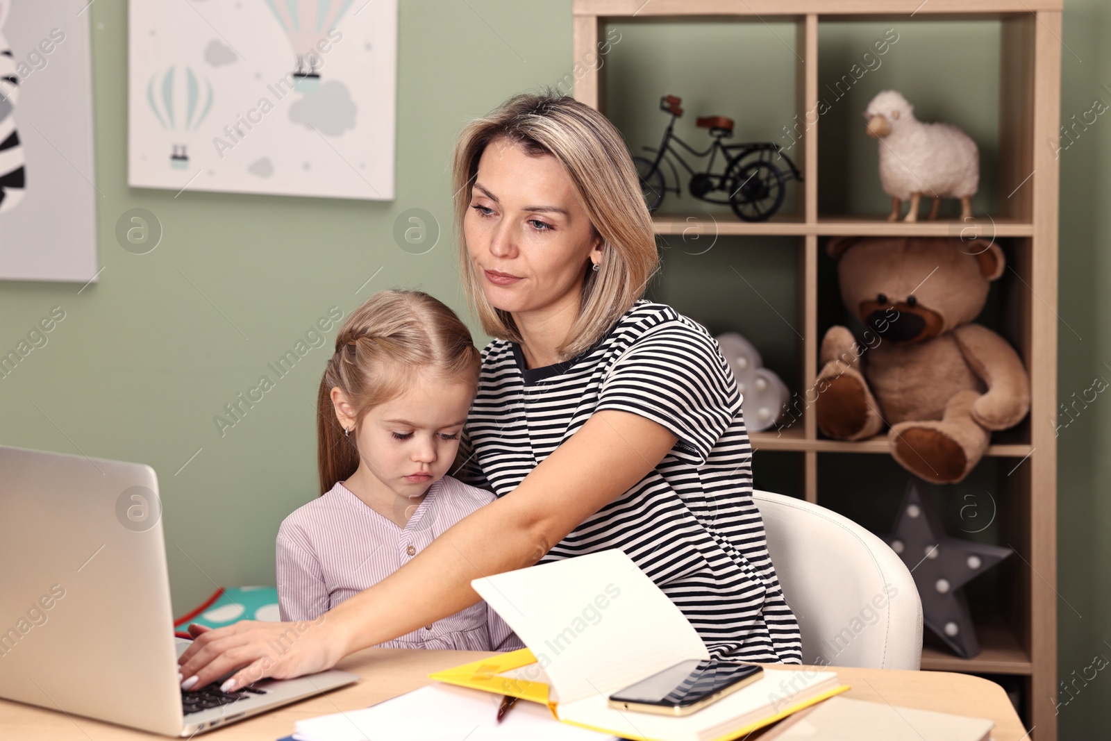 Photo of Overwhelmed single mother working with laptop and her daughter at table in child's room