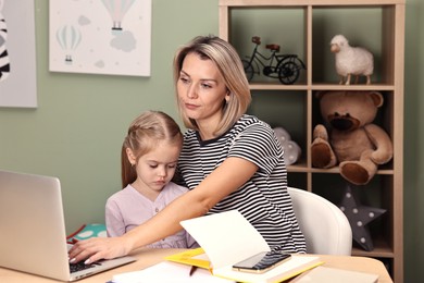 Photo of Overwhelmed single mother working with laptop and her daughter at table in child's room