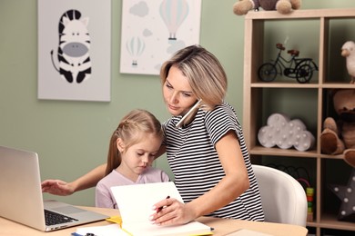 Photo of Work-family balance. Overwhelmed single mother talking by smartphone and her daughter at table in child's room