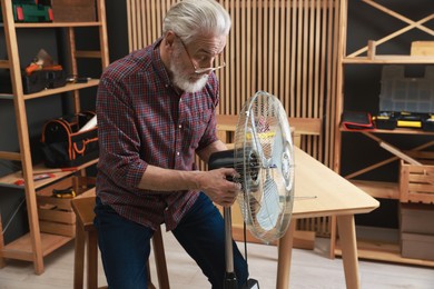 Photo of Relaxing hobby. Senior man repairing fan in workshop