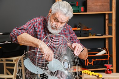 Photo of Relaxing hobby. Senior man repairing fan with screwdriver in workshop