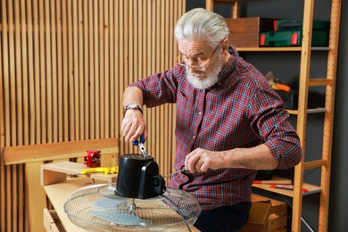 Photo of Relaxing hobby. Senior man repairing fan in workshop