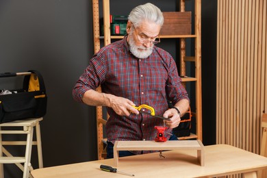 Photo of Relaxing hobby. Senior man with hacksaw and vise assembling wooden shelf in workshop