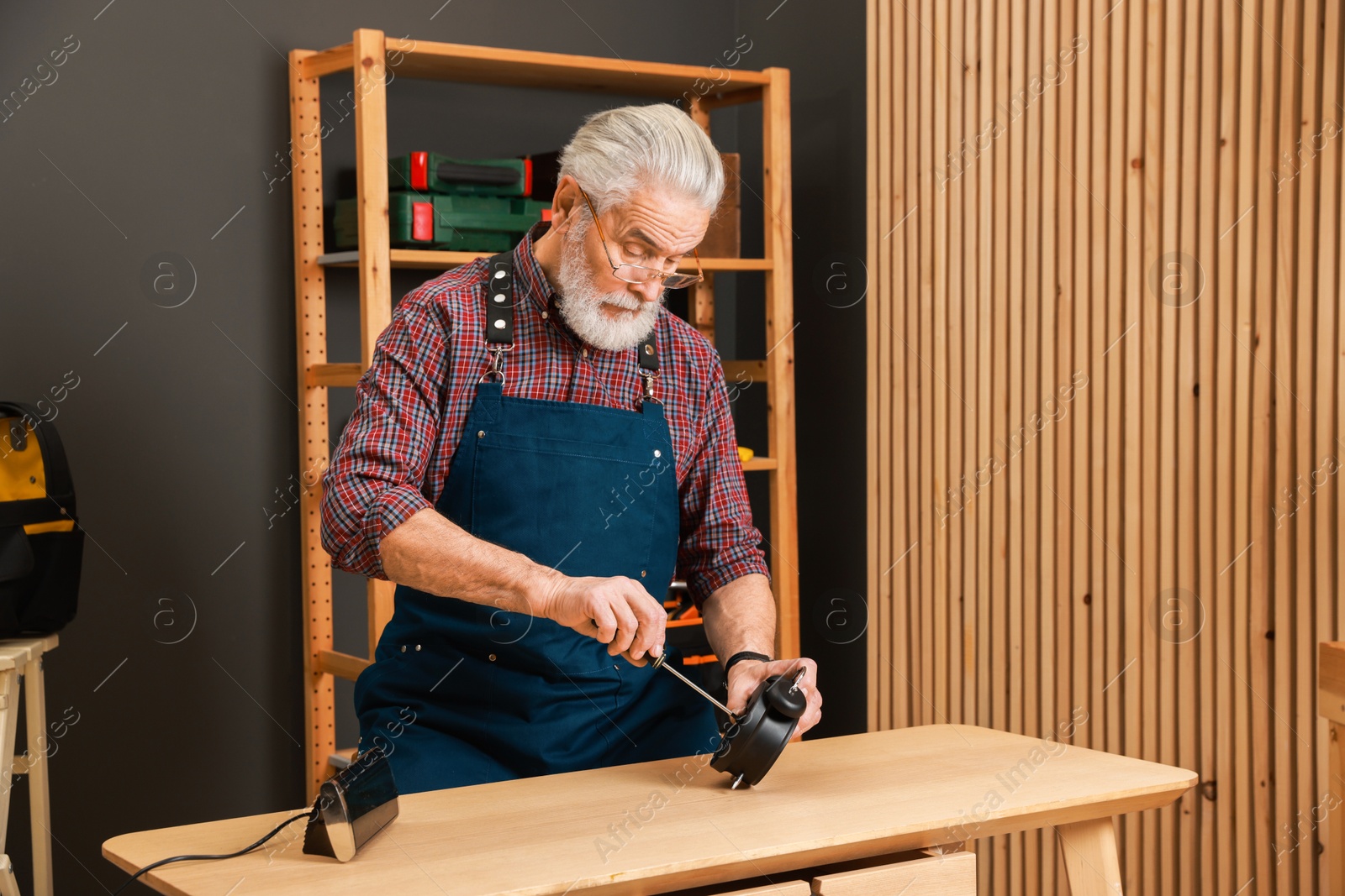 Photo of Relaxing hobby. Senior man repairing alarm clock at wooden table in workshop