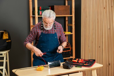 Photo of Relaxing hobby. Senior man testing alarm clock with multimeter in workshop