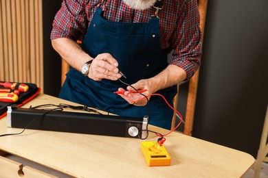 Photo of Relaxing hobby. Senior man testing soundbar with multimeter in workshop, closeup