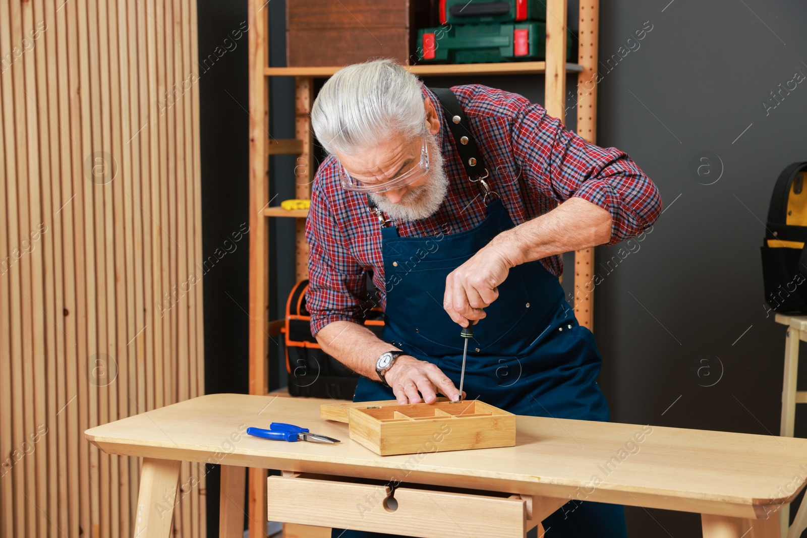 Photo of Relaxing hobby. Senior man repairing wooden jewelry box with screwdriver in workshop