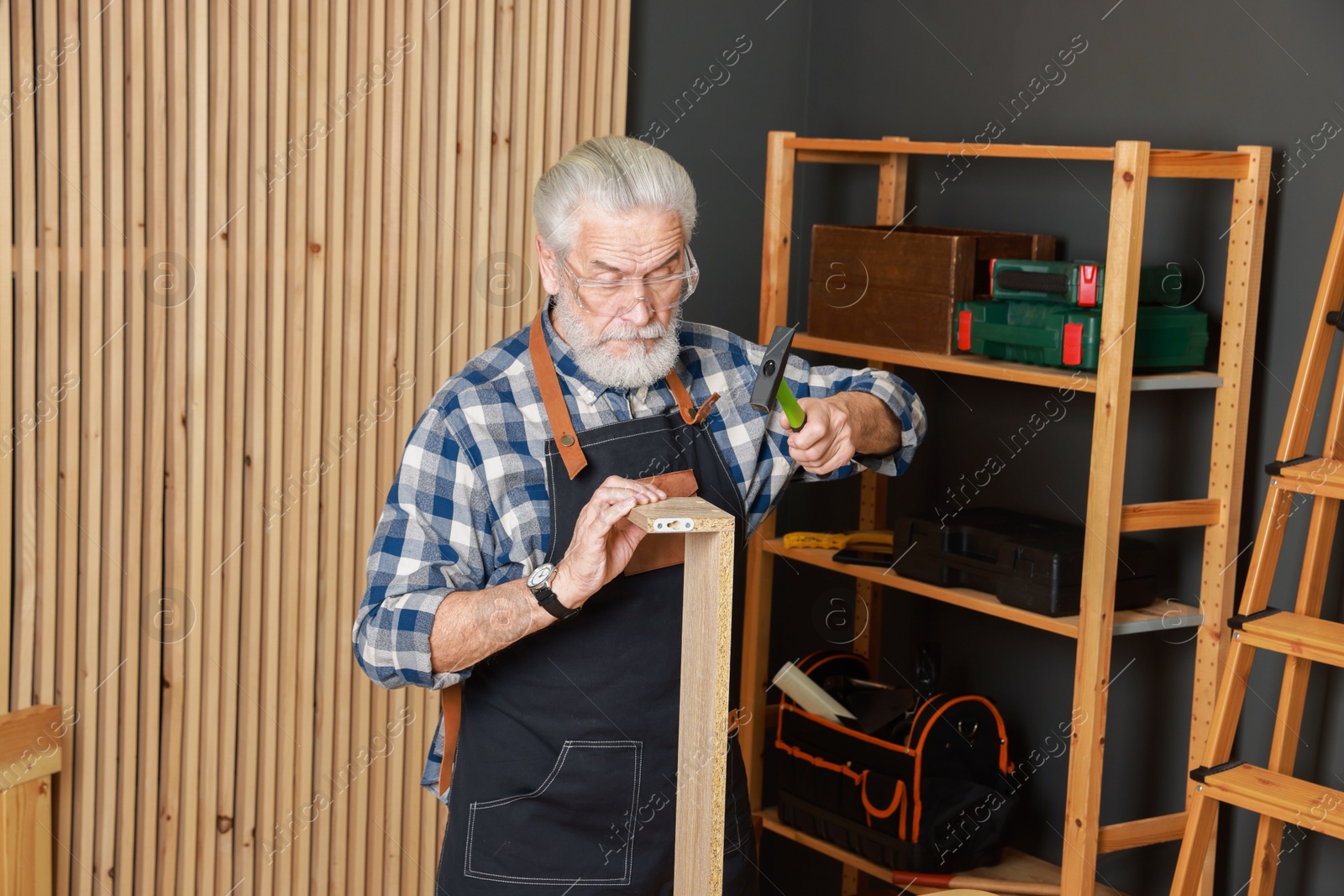 Photo of Relaxing hobby. Senior man repairing wooden shelf with hammer in workshop