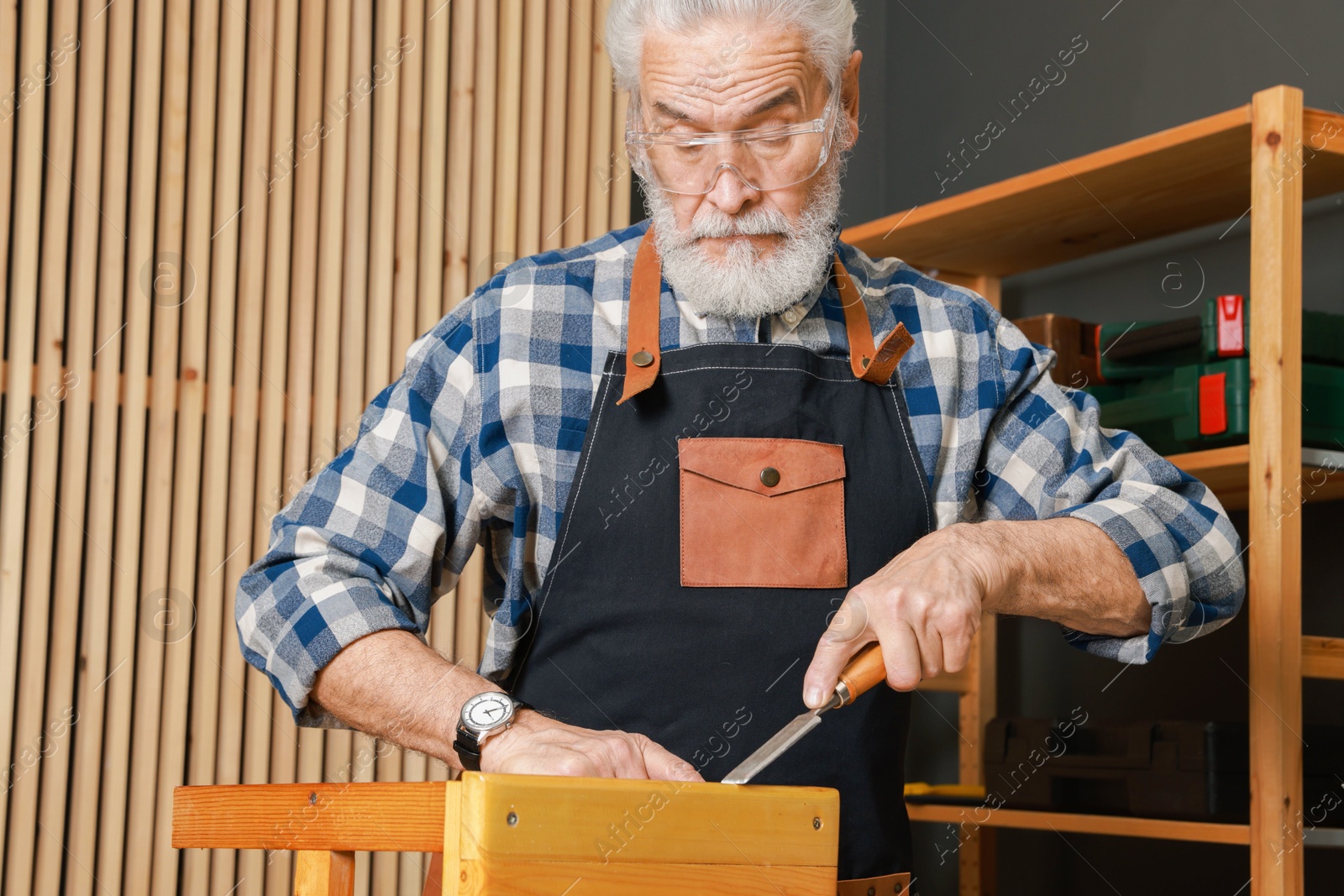 Photo of Relaxing hobby. Senior man repairing wooden stool with chisel in workshop