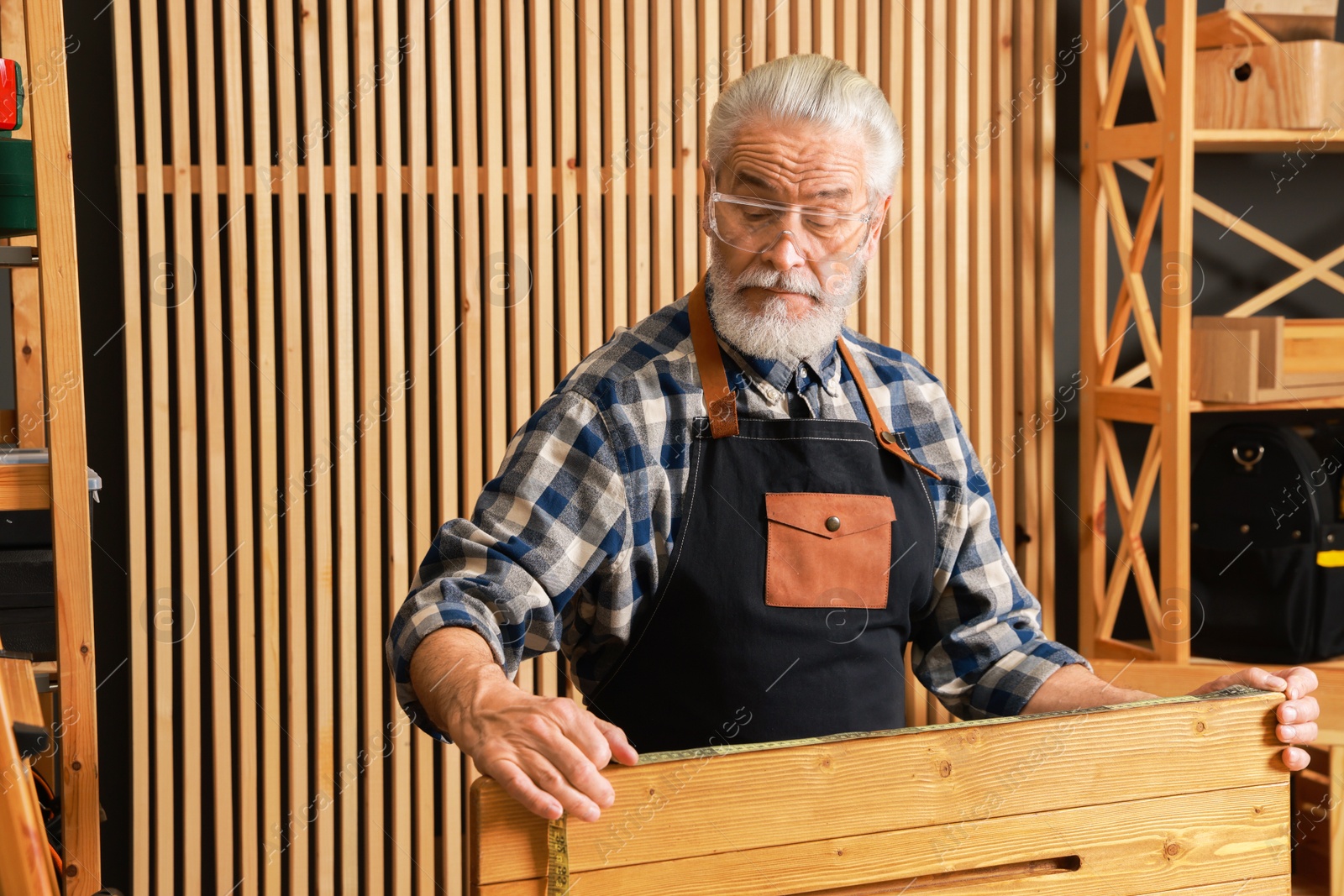 Photo of Relaxing hobby. Senior man measuring wooden plank with tape in workshop