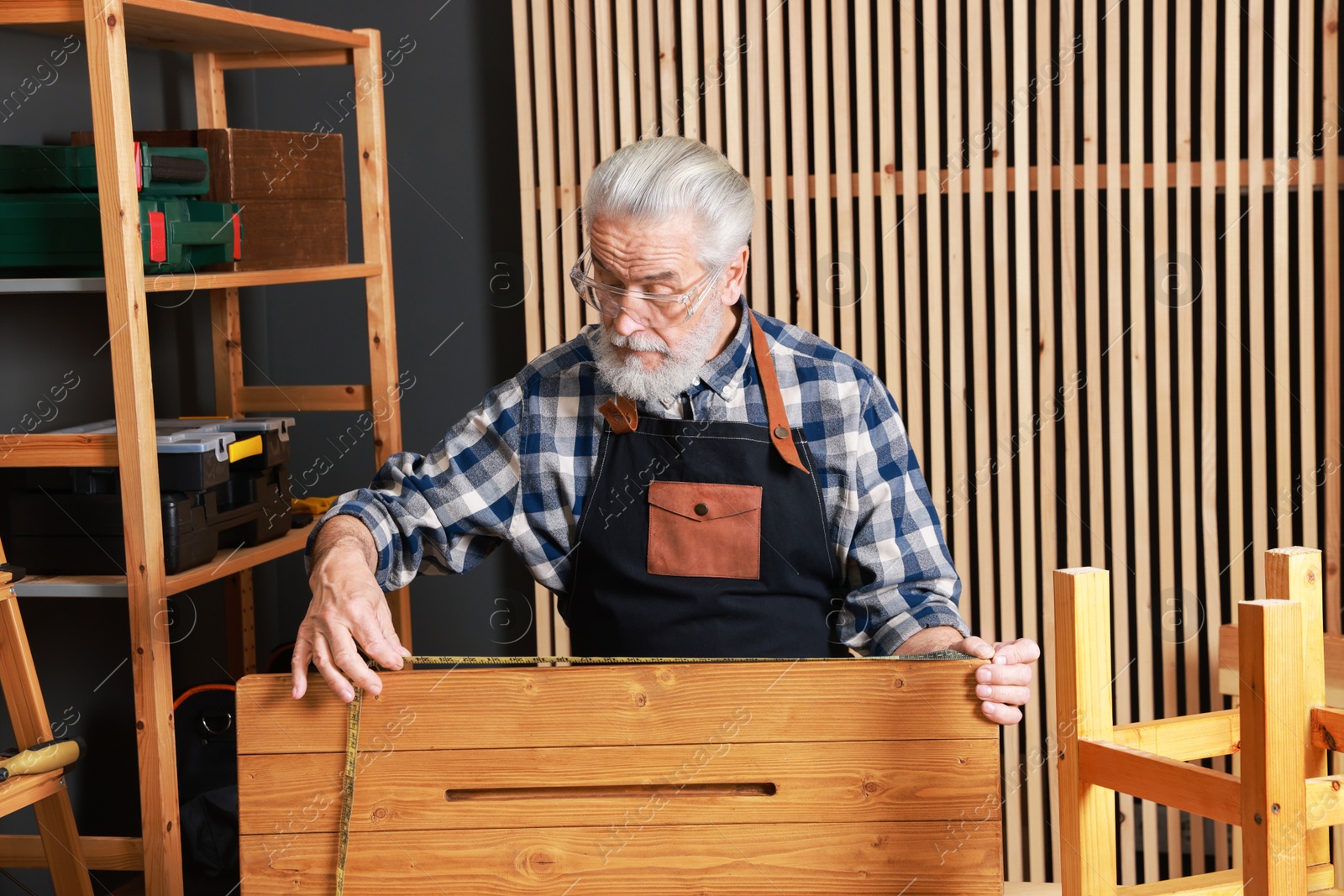 Photo of Relaxing hobby. Senior man measuring wooden plank with tape in workshop