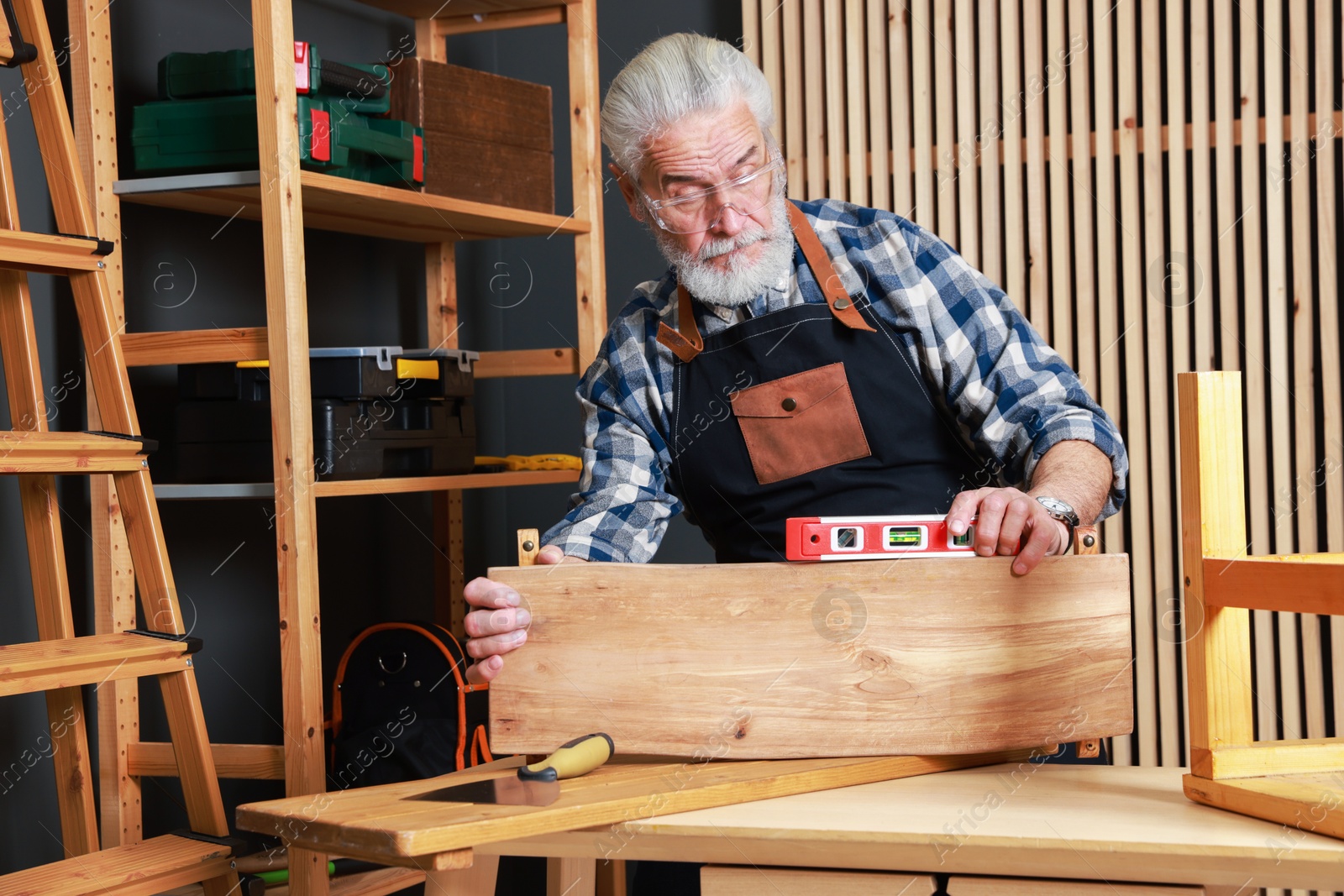 Photo of Relaxing hobby. Senior man working with wooden plank and level tool at table in workshop