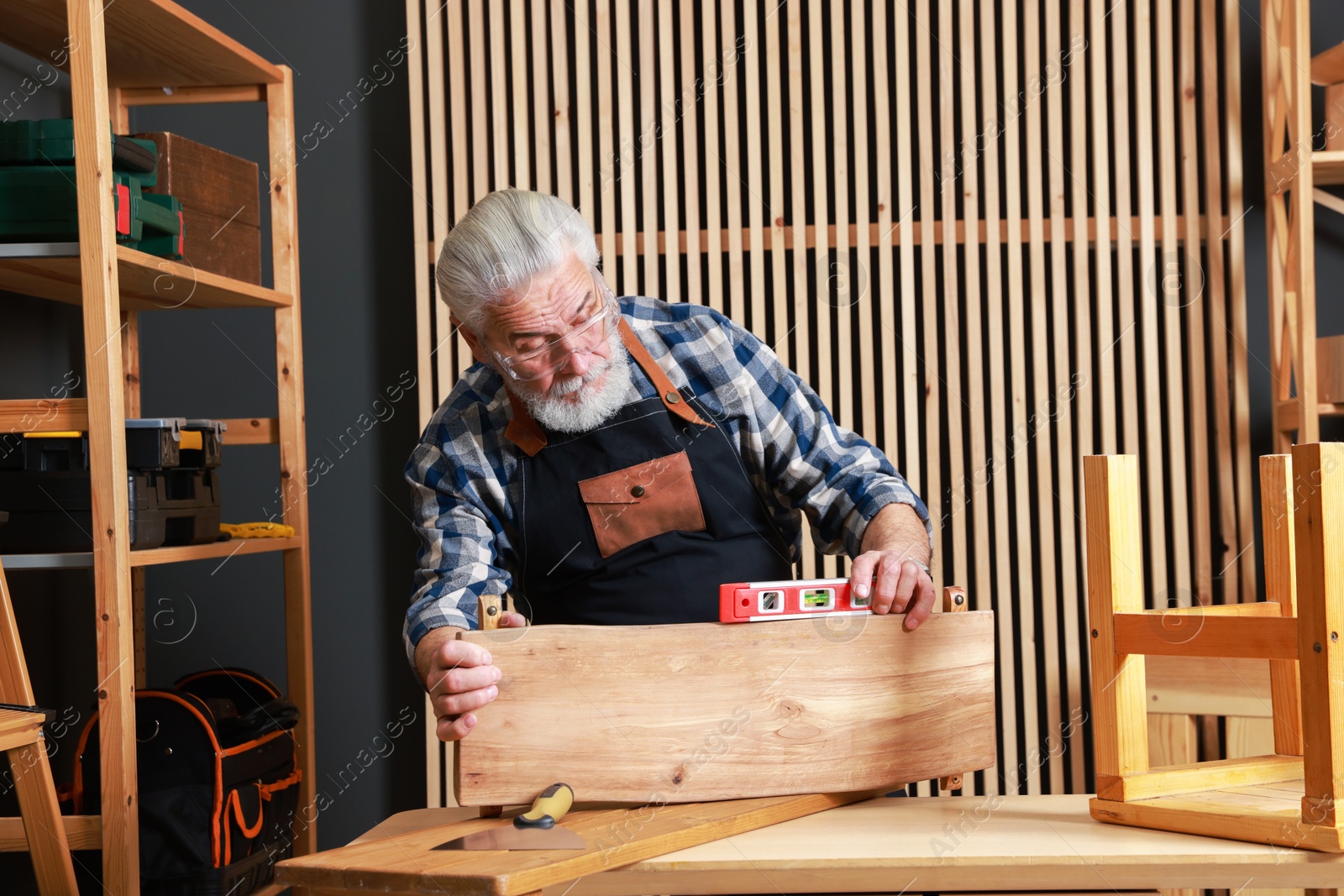 Photo of Relaxing hobby. Senior man working with wooden plank and level tool at table in workshop