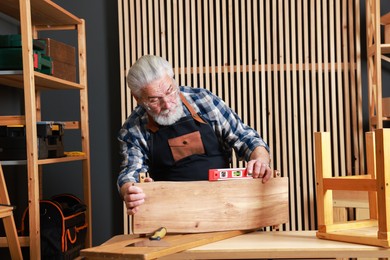 Photo of Relaxing hobby. Senior man working with wooden plank and level tool at table in workshop