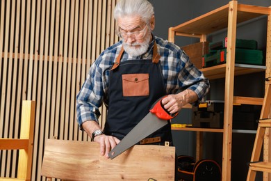 Photo of Relaxing hobby. Senior man working with wooden plank and saw in workshop