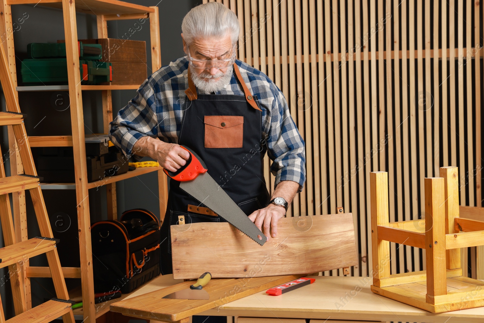 Photo of Relaxing hobby. Senior man working with wooden plank and saw in workshop