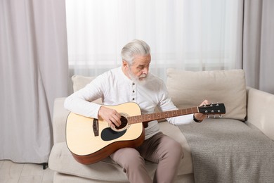 Photo of Relaxing hobby. Senior man playing guitar on sofa at home