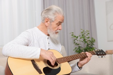 Photo of Relaxing hobby. Senior man playing guitar on sofa at home