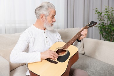 Photo of Relaxing hobby. Senior man playing guitar on sofa at home