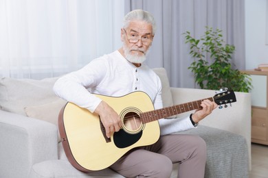 Photo of Relaxing hobby. Senior man playing guitar on sofa at home