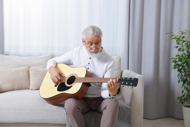 Photo of Relaxing hobby. Senior man playing guitar on sofa at home