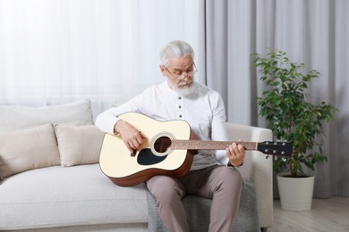 Photo of Relaxing hobby. Senior man playing guitar on sofa at home