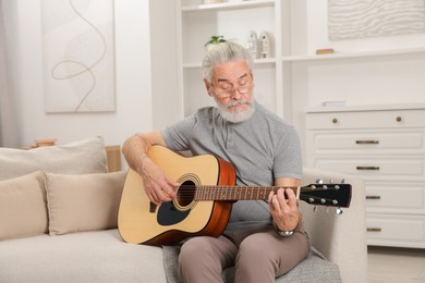 Photo of Relaxing hobby. Senior man playing guitar on sofa at home