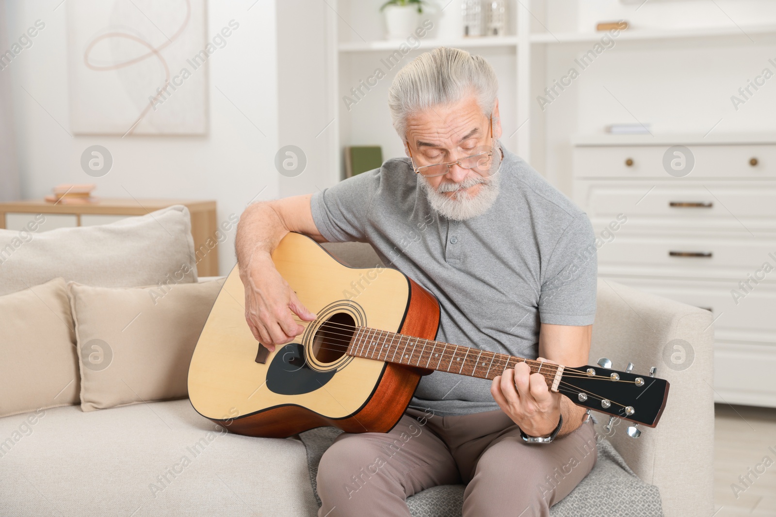 Photo of Relaxing hobby. Senior man playing guitar on sofa at home