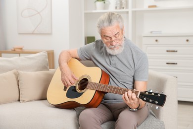 Photo of Relaxing hobby. Senior man playing guitar on sofa at home