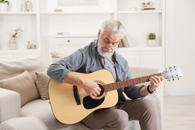 Photo of Relaxing hobby. Senior man playing guitar on sofa at home