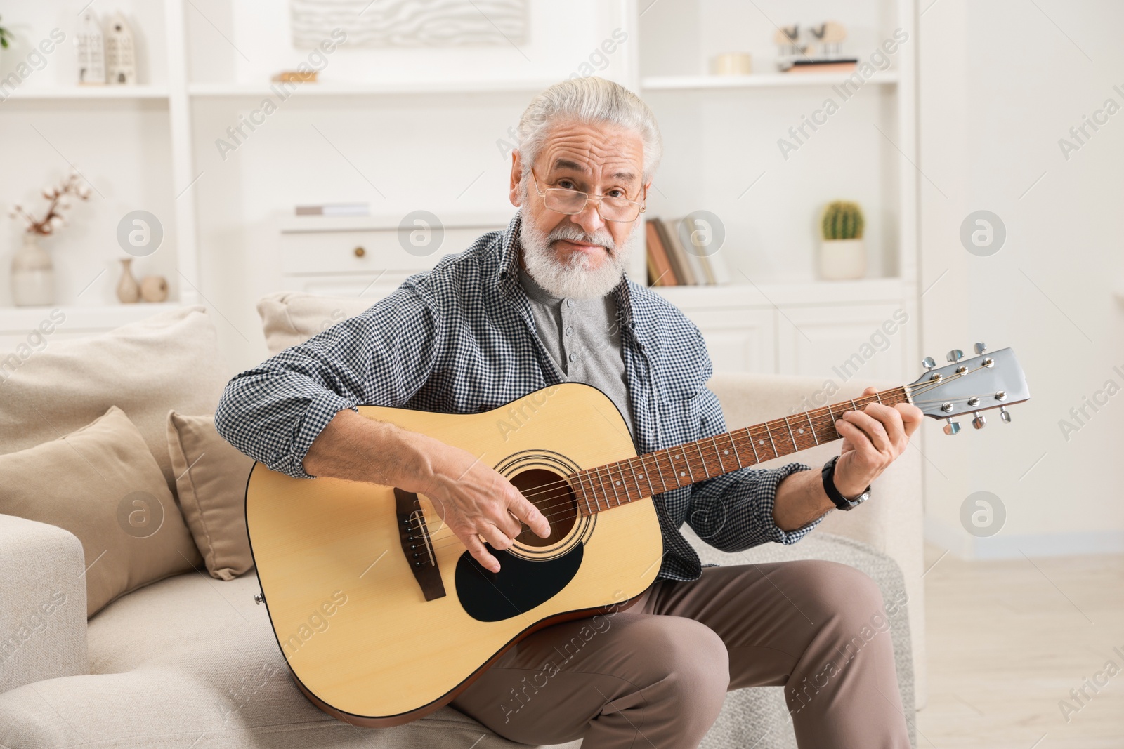 Photo of Relaxing hobby. Senior man playing guitar on sofa at home