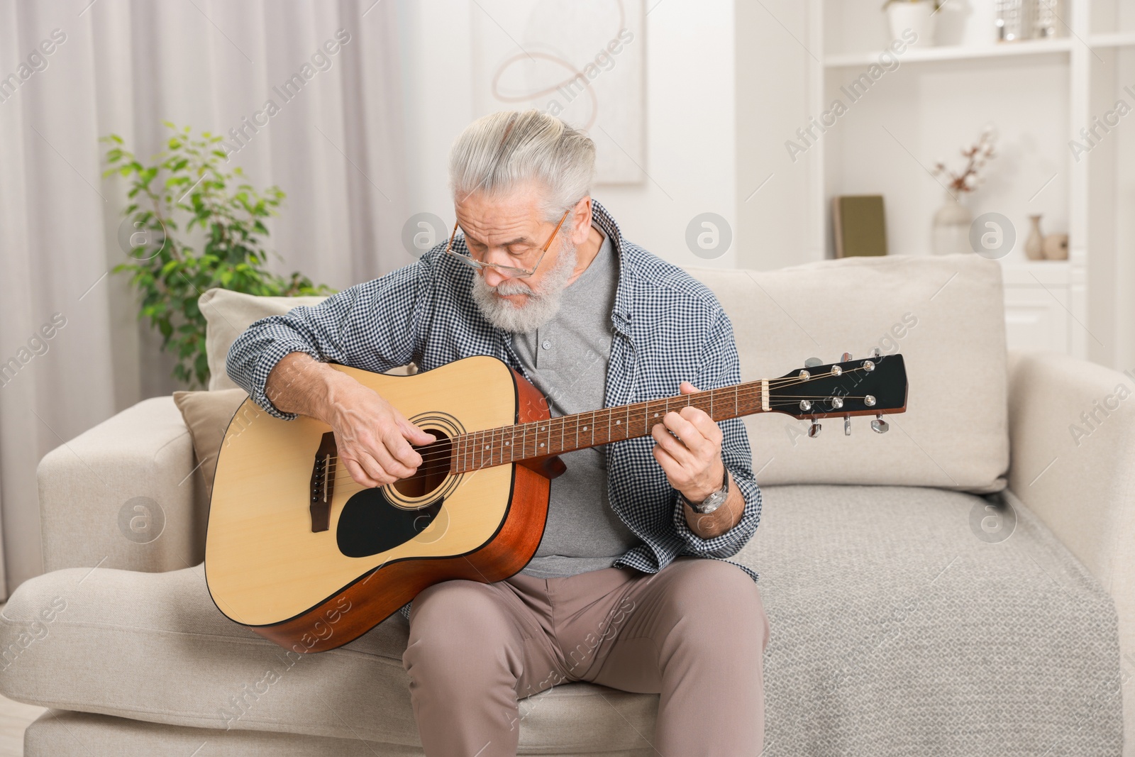 Photo of Relaxing hobby. Senior man playing guitar on sofa at home